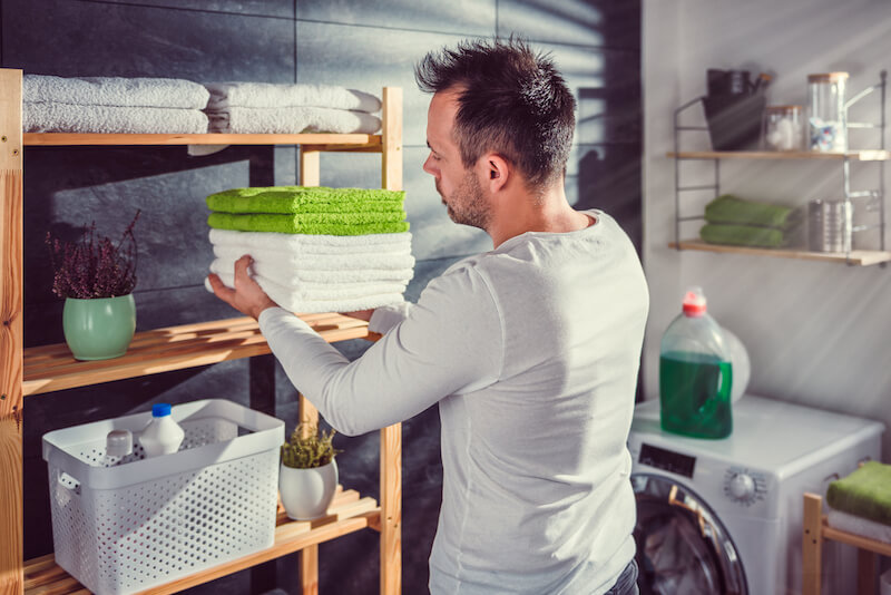 Men wearing white shirt arranging clean green towels at laundry room
